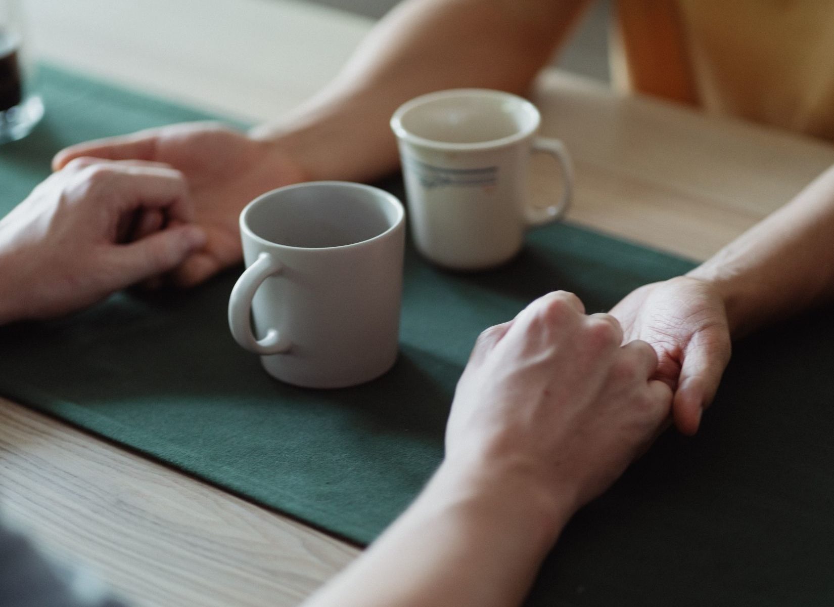 Couple holding hands across a table with mugs between them