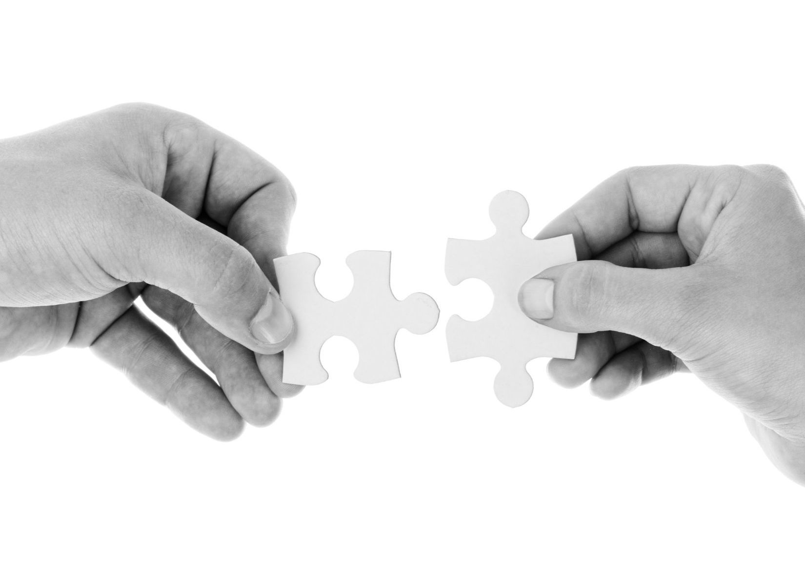 Two puzzle pieces being held by two hands in black and white